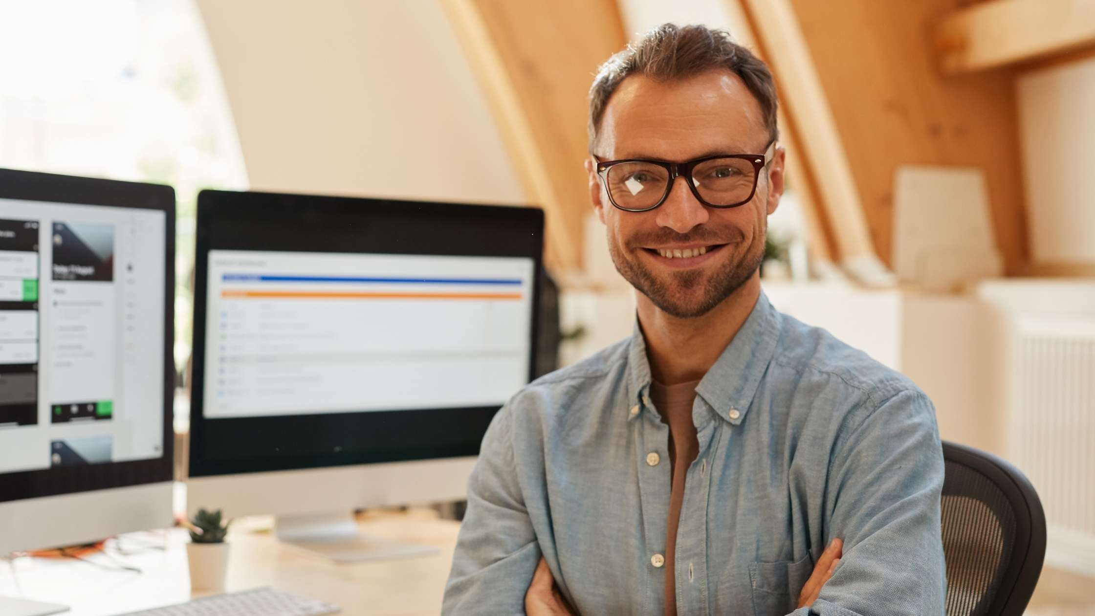 Smiling professional at a desk with dual monitors showing contract software.