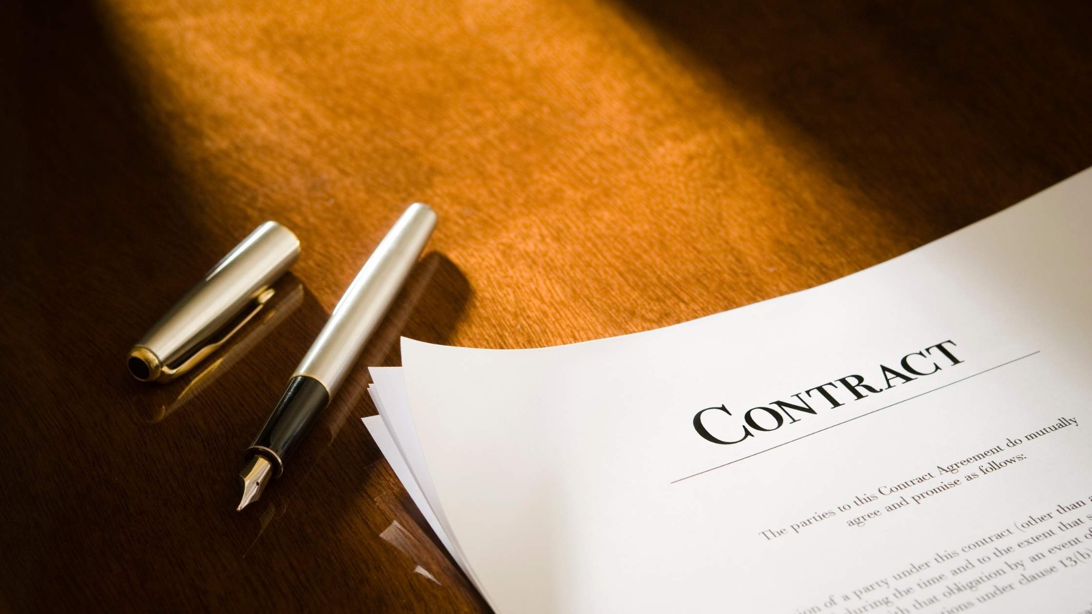 Fountain pen beside a standard contract on a wooden desk.
