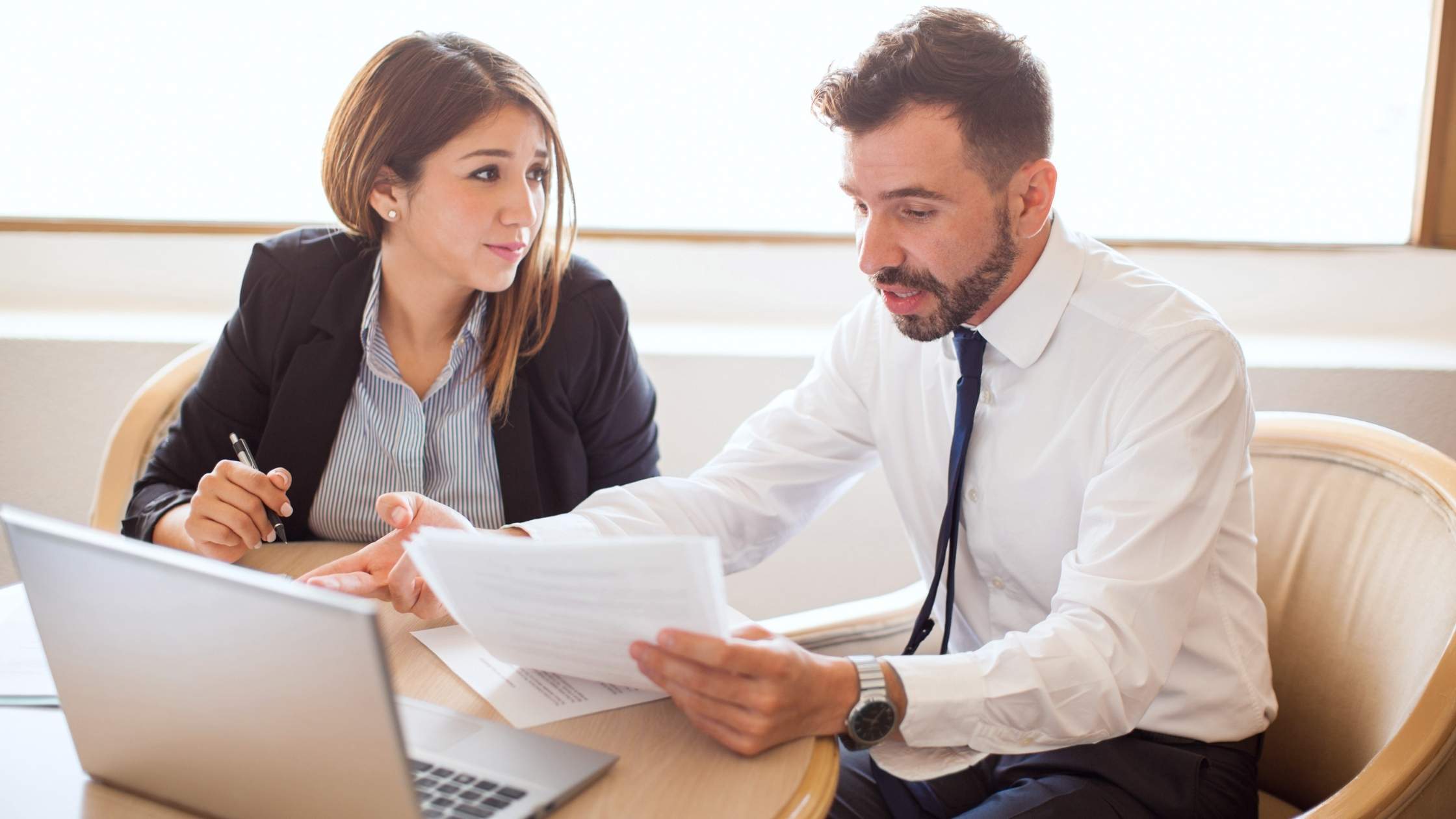 Two colleagues discussing the purpose of a contract and smiling across a desk.