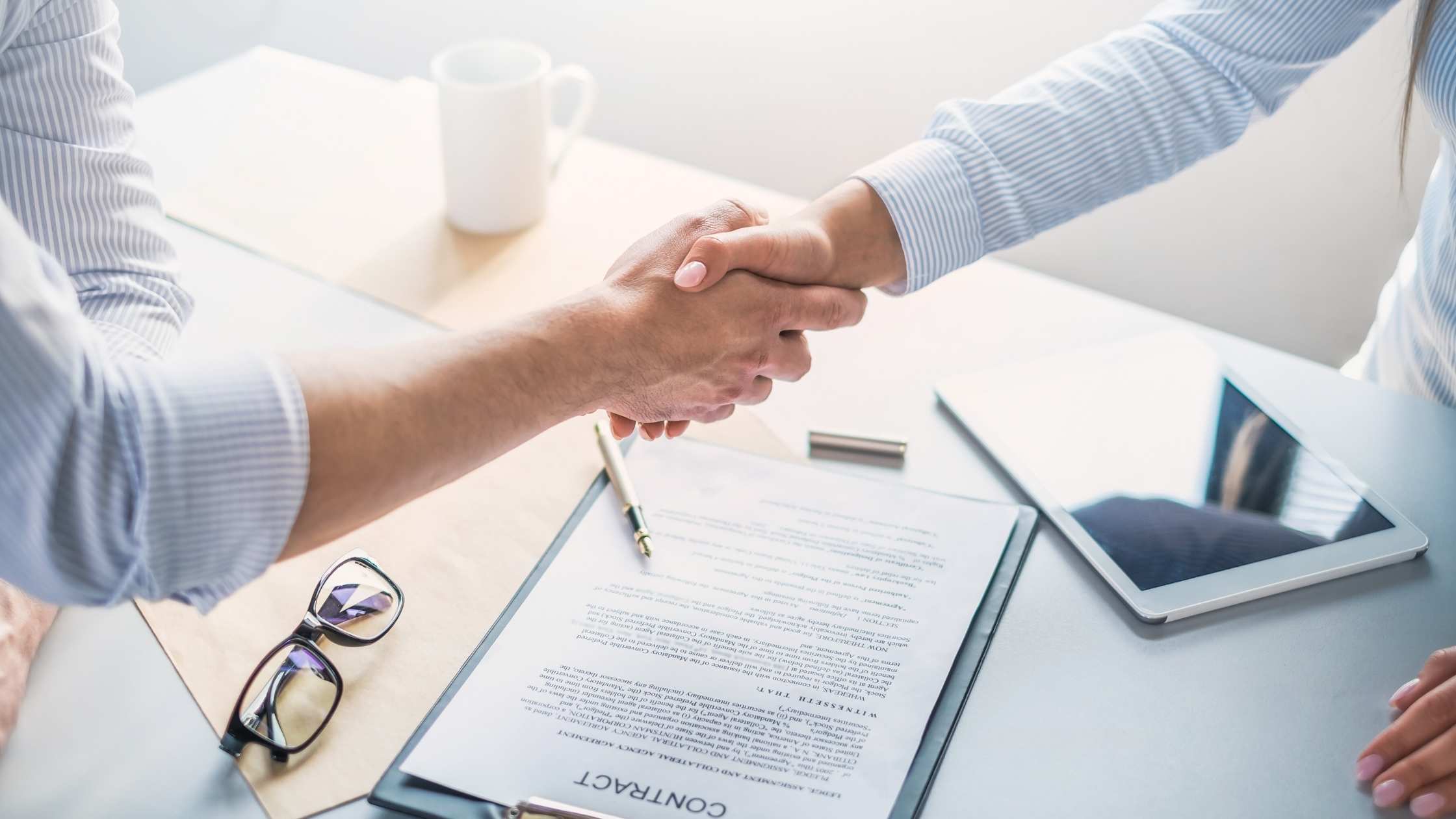 Close-up of a handshake over a signed contract on a desk which was previously an agreement